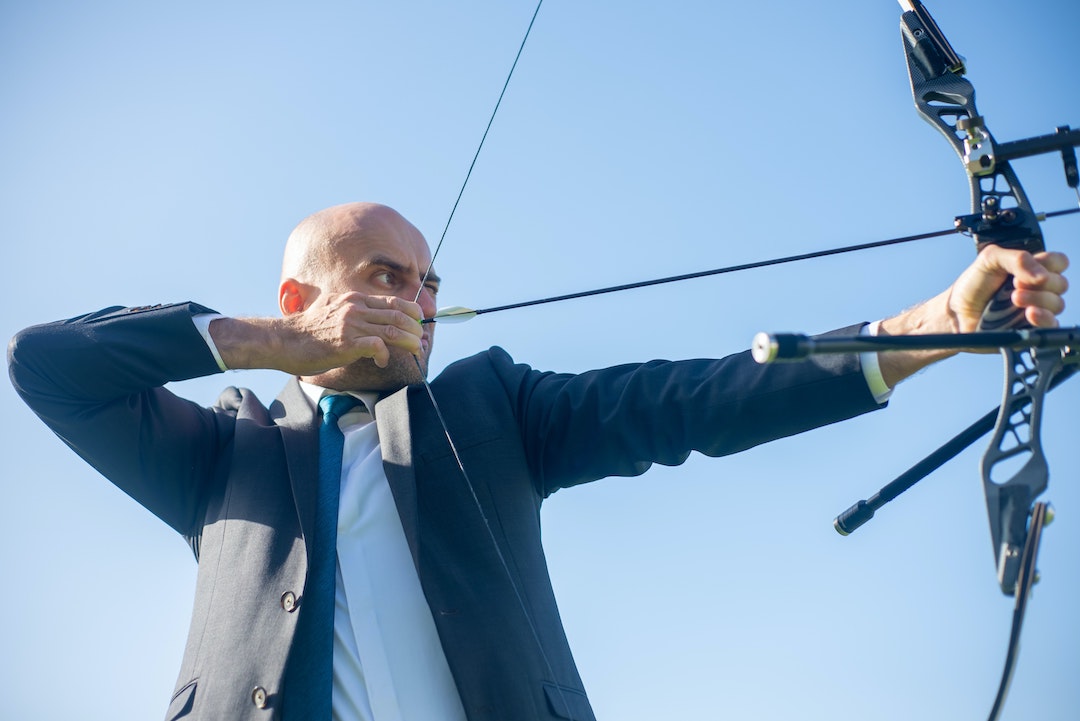 Uomo in giacca e cravatta che si allena al tiro con l'arco - Foto di Kampus Production su Pexels